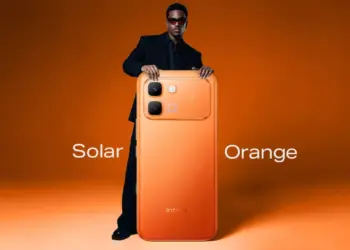 Pria dengan kacamata hitam memegang HP 4 Jutaan Infinix varian warna Solar Orange.