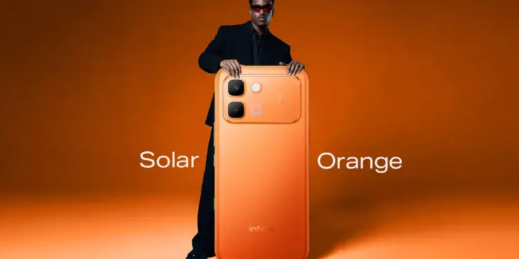 Pria dengan kacamata hitam memegang HP 4 Jutaan Infinix varian warna Solar Orange.
