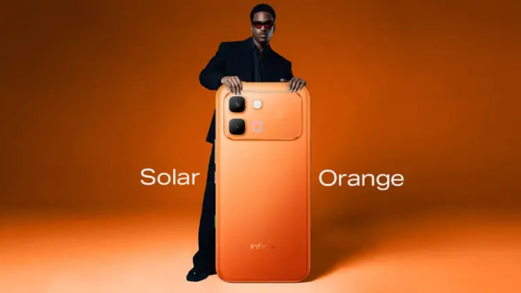 Pria dengan kacamata hitam memegang HP 4 Jutaan Infinix varian warna Solar Orange.