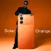 Pria dengan kacamata hitam memegang HP 4 Jutaan Infinix varian warna Solar Orange.