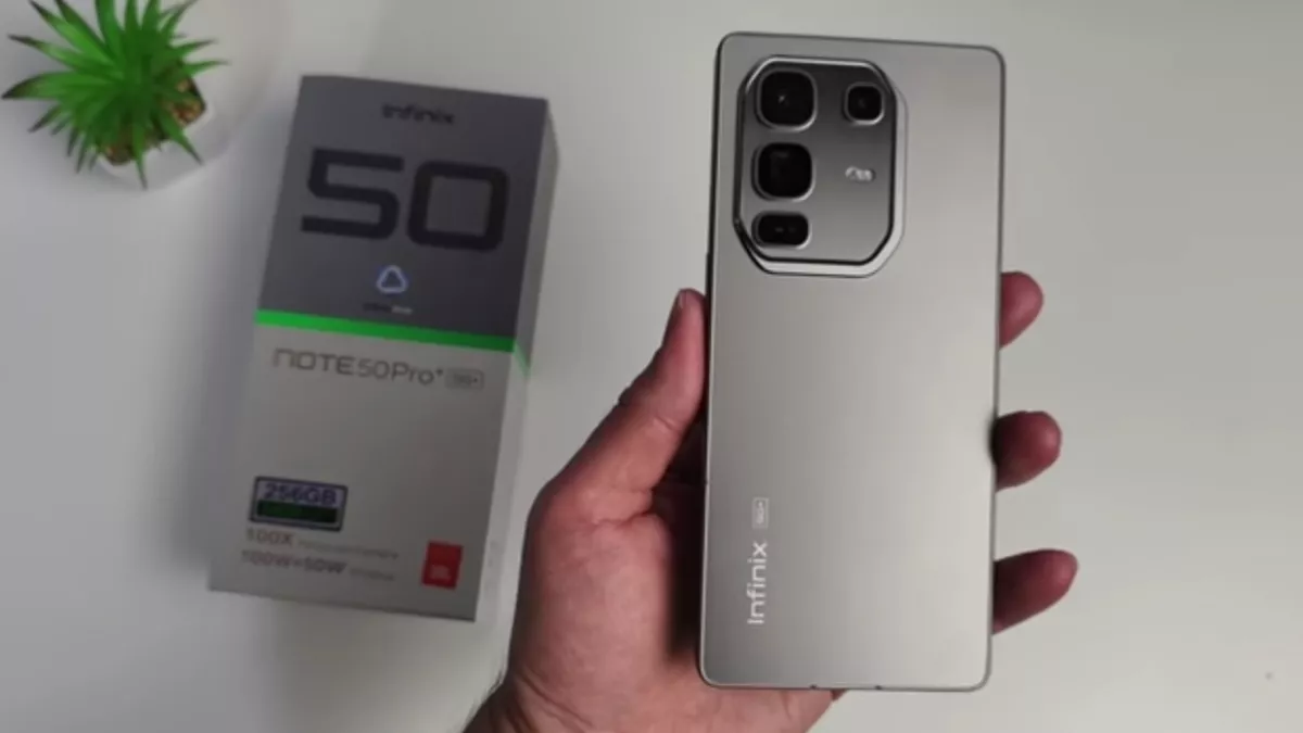 Seseorang memegang Infinix Note 50 Pro 5G berwarna silver beserta dus kemasannya di latar belakang.