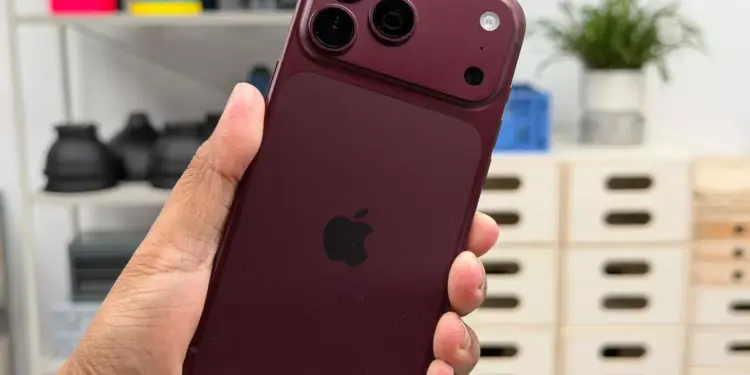 Seseorang menggenggam iPhone 18 Pro warna merah marun dengan desain modul kamera baru yang mendukung fitur anti foto AI.
