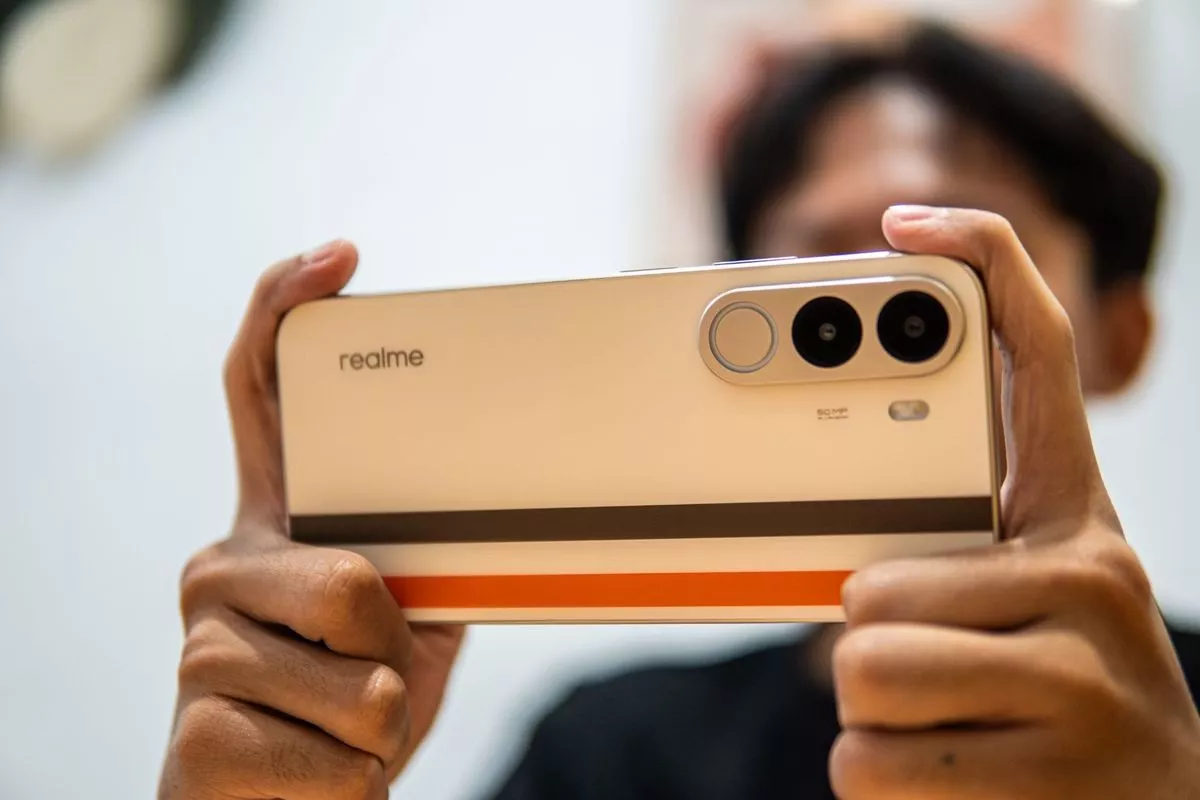 Seseorang memegang HP Realme 2 jutaan dengan desain bodi emas bergaris saat posisi horisontal.