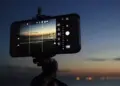 Smartphone terpasang di tripod memotret pemandangan matahari terbenam dengan mode manual kamera