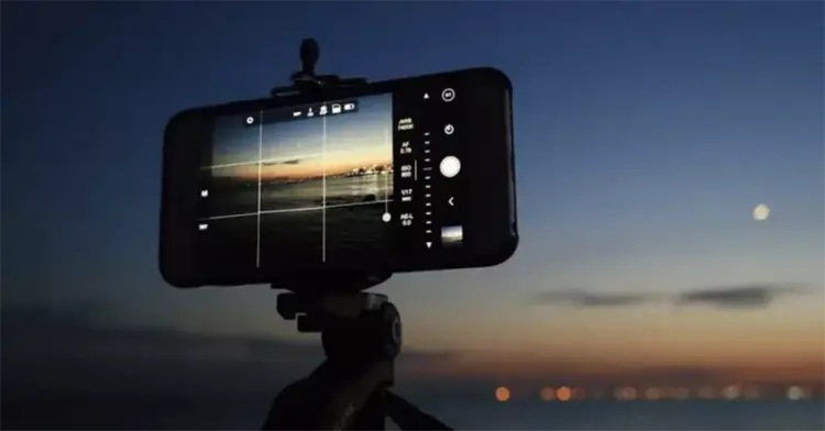 Smartphone terpasang di tripod memotret pemandangan matahari terbenam dengan mode manual kamera