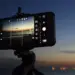Smartphone terpasang di tripod memotret pemandangan matahari terbenam dengan mode manual kamera