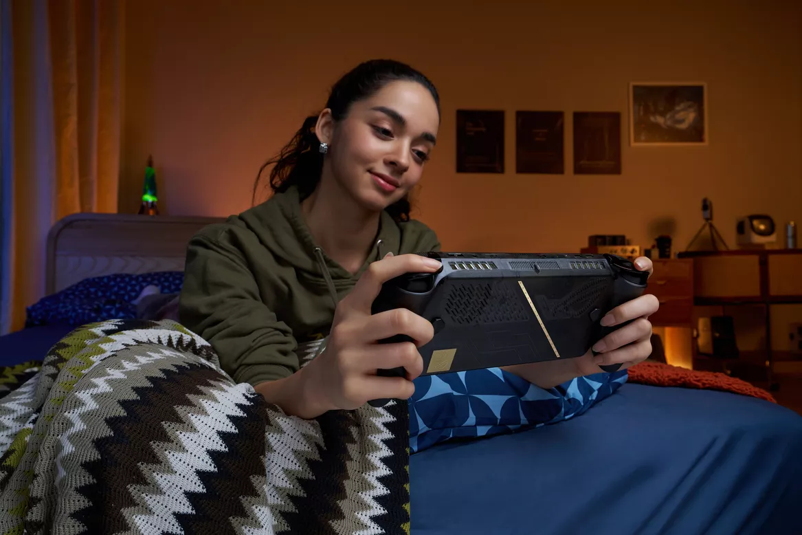 Seorang wanita memainkan perangakat handheld gaming ROG Xbox Ally X20 di tempat tidur dengan nyaman.