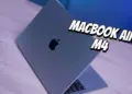 Tampilan fisik MacBook Air M4 berwarna abu-abu yang terbuka di atas meja kayu dengan pencahayaan biru.