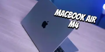 Tampilan fisik MacBook Air M4 berwarna abu-abu yang terbuka di atas meja kayu dengan pencahayaan biru.