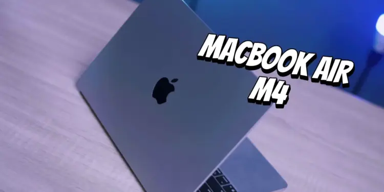 Tampilan fisik MacBook Air M4 berwarna abu-abu yang terbuka di atas meja kayu dengan pencahayaan biru.