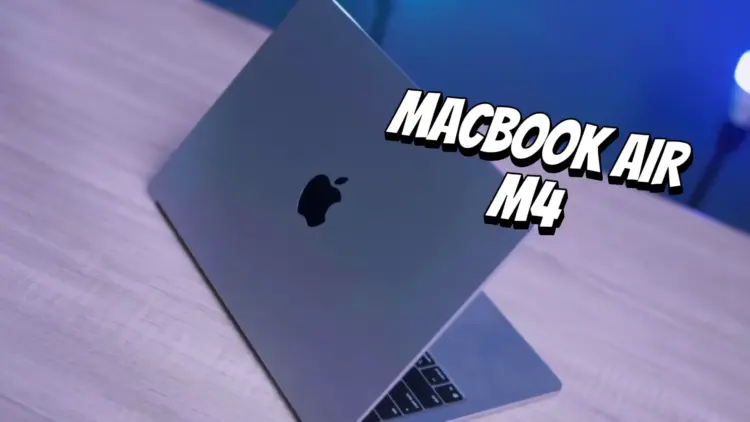 Tampilan fisik MacBook Air M4 berwarna abu-abu yang terbuka di atas meja kayu dengan pencahayaan biru.