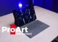Laptop hibrida detachable ASUS ProArt PZ14 berwarna abu-abu tua di atas meja kayu dengan pencahayaan studio biru cobalt.