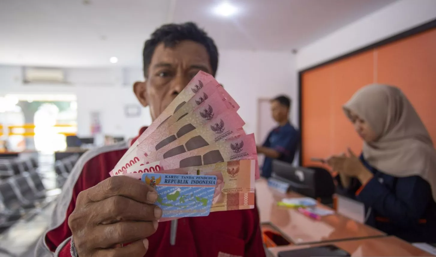 Penerima bantuan menunjukkan uang tunai dan KTP saat pencairan BSU Kemenaker 2026 di kantor pos