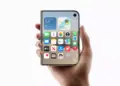 Tangan memegang perangkat iPhone Duo dengan layar depan persegi yang menampilkan antarmuka iOS.