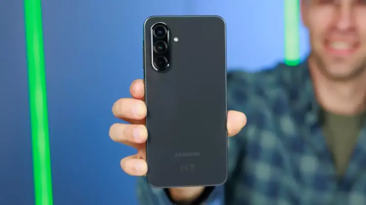 Tangan memegang HP Samsung 5G berwarna hitam memperlihatkan modul tiga kamera belakang.