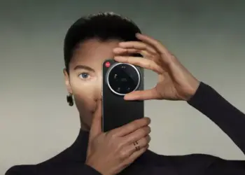 Seorang wanita memegang HP Kamera Leica berwarna hitam tepat di depan wajahnya.