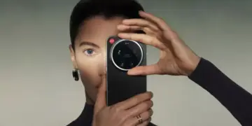 Seorang wanita memegang HP Kamera Leica berwarna hitam tepat di depan wajahnya.