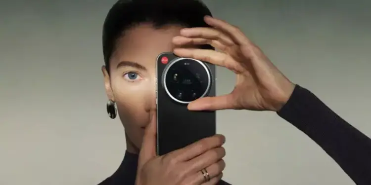 Seorang wanita memegang HP Kamera Leica berwarna hitam tepat di depan wajahnya.