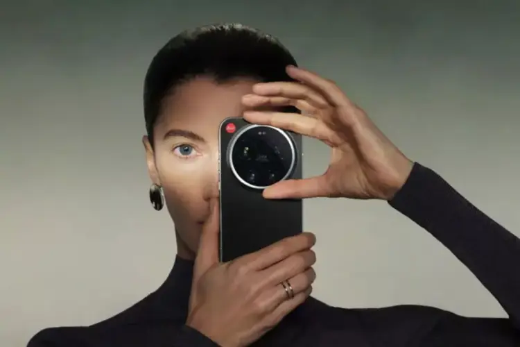 Seorang wanita memegang HP Kamera Leica berwarna hitam tepat di depan wajahnya.