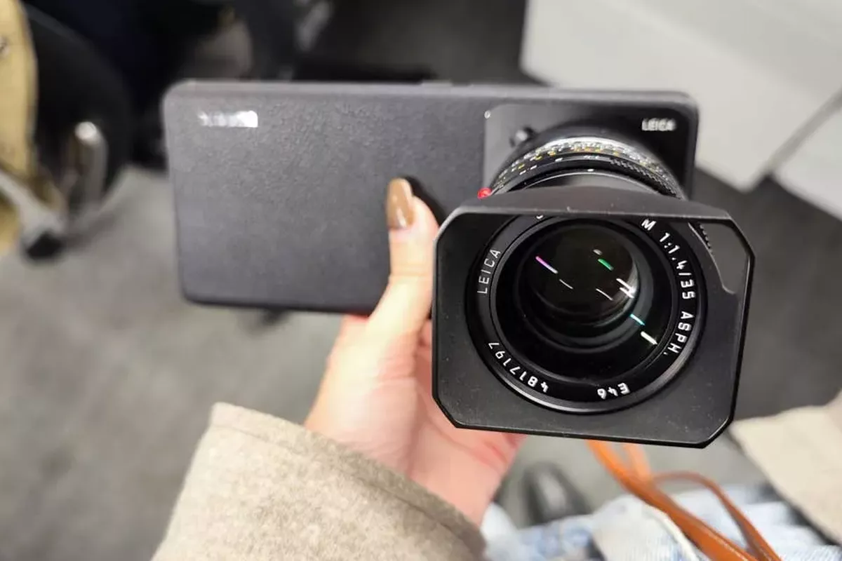 Tangan memegang HP Kamera Leica yang terpasang lensa eksternal Leica M 35mm ASPH.