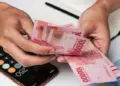 Tangan pekerja menghitung lembaran uang tunai rupiah BSU Kemenaker 2026 di dekat kalkulator ponsel