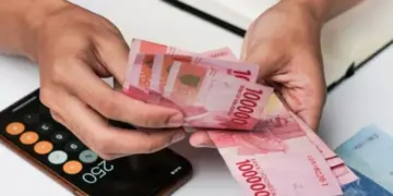 Tangan pekerja menghitung lembaran uang tunai rupiah BSU Kemenaker 2026 di dekat kalkulator ponsel