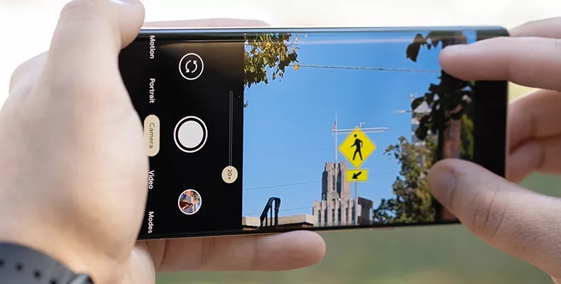 Seseorang menggunakan HP kamera zoom 20x untuk membidik rambu lalu lintas dan bangunan dari jarak jauh.