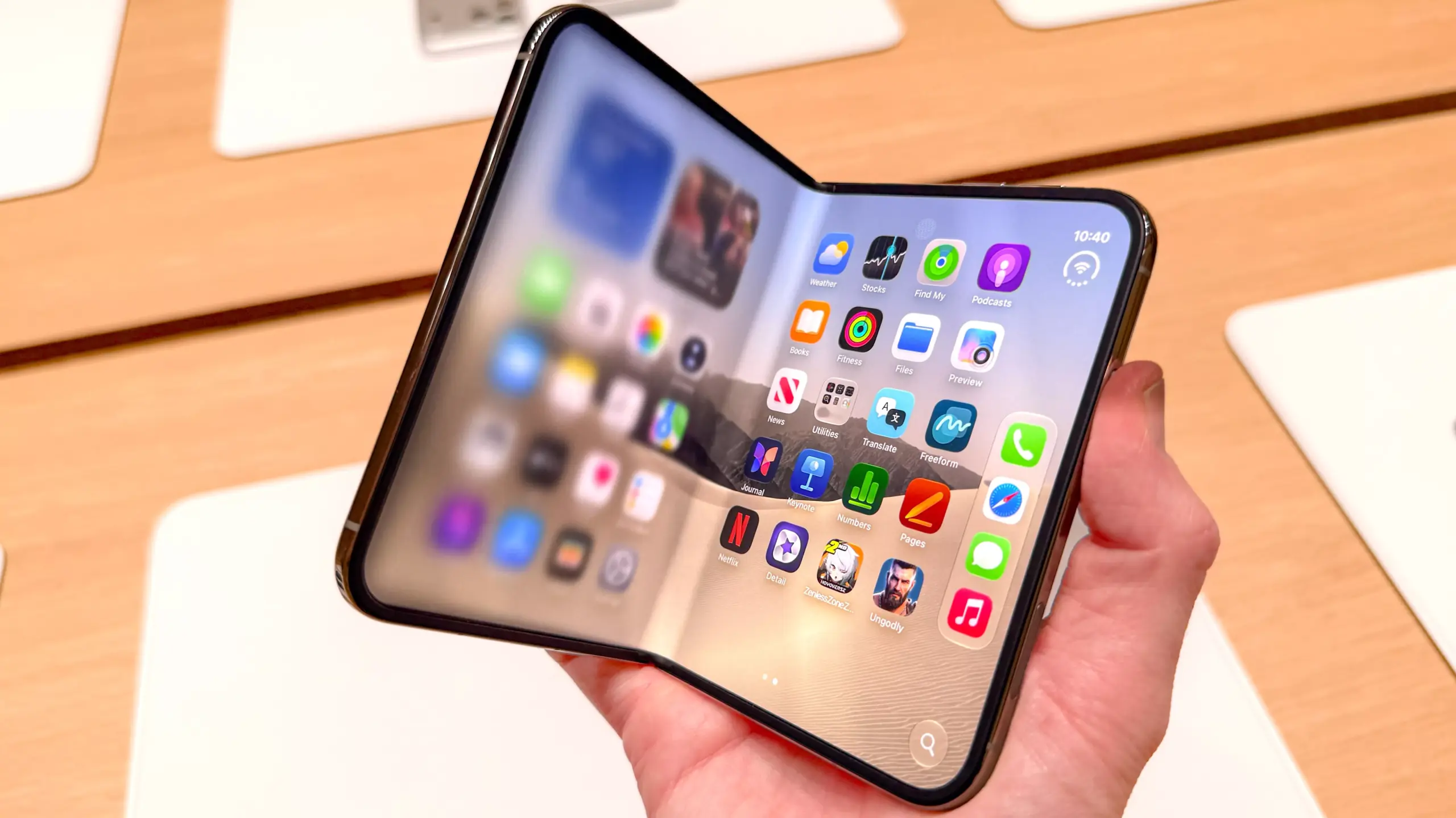Tangan memegang smartphone lipat iPhone Duo yang sedikit terlipat menampilkan antarmuka iOS
