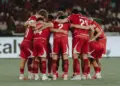 Timnas Indonesia berkumpul di tengah lapangan, saling merangkul, menciptakan momen persatuan yang kuat.