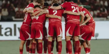 Timnas Indonesia berkumpul di tengah lapangan, saling merangkul, menciptakan momen persatuan yang kuat.