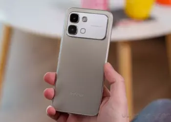 Tangan memegang bodi belakang HP Infinix warna silver dengan modul kamera 50MP.