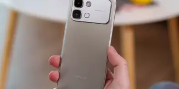 Tangan memegang bodi belakang HP Infinix warna silver dengan modul kamera 50MP.