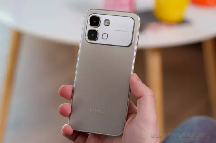 Tangan memegang bodi belakang HP Infinix warna silver dengan modul kamera 50MP.