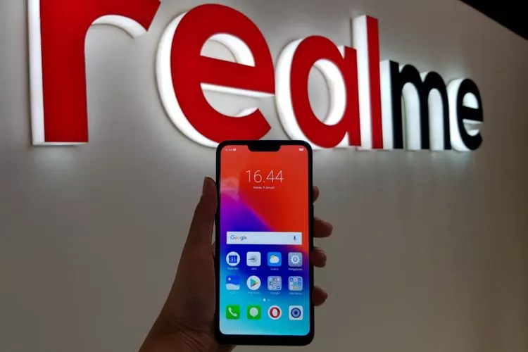 Seseorang menggenggam smartphone realme di depan logo merek realme