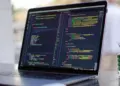 Layar laptop menampilkan baris kode pemrograman HTML dan CSS untuk kebutuhan mahasiswa informatika
