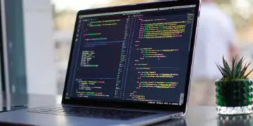 Layar laptop menampilkan baris kode pemrograman HTML dan CSS untuk kebutuhan mahasiswa informatika