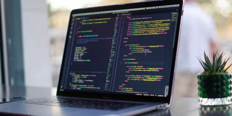 Layar laptop menampilkan baris kode pemrograman HTML dan CSS untuk kebutuhan mahasiswa informatika